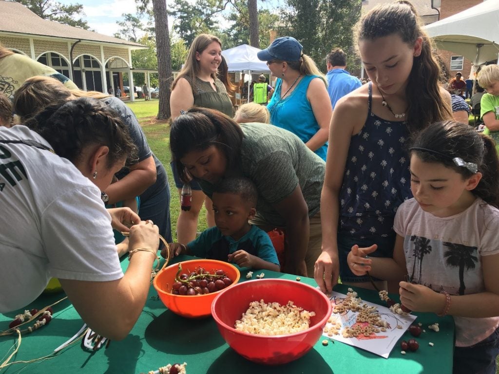 Outreach Coordinator Helen Rose Patterson helps kids string bird snacks onto pipe cleaners. 